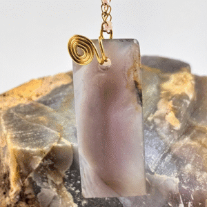 Detalle en macro de colgante rectangular de calcedonia lila con engaste en espiral de alambre dorado en la parte superior.