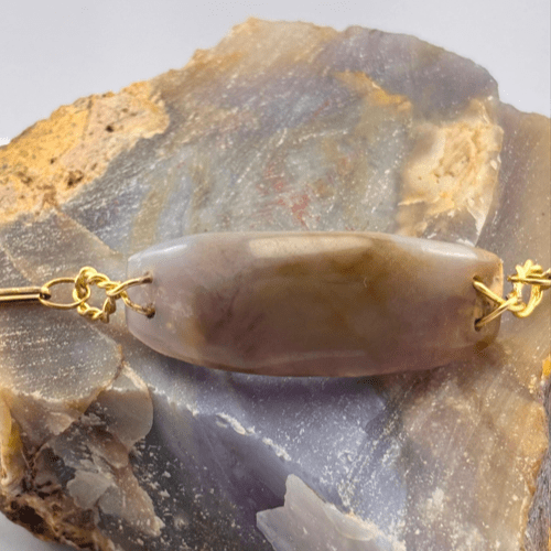 Detalle de la piedra central ovalada y plana de Calcedonia morada clara, con engaste de alambre dorado conectado a la cadena de la pulsera.