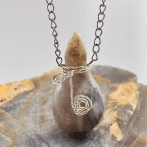 Colgante de Calcedonia pulida en forma de jicaro , engarzado en alambrismo con espirales, colgando de una cadena plateada.