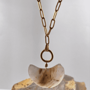 Colgante de Calcedonia en forma de media luna, conectado a un aro dorado y una cadena dorada de eslabones grandes, flotando sobre mineral de calcedonia en bruto.