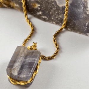 Collar con colgante de Calcedonia rectangular en tonos morados y blancos, engarzado en alambre dorado, sobre cadena dorada y roca.