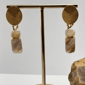 Aretes con poste circular dorado y piedra cilíndrica de amatista o ágata con bandas, en exhibidor de joyería.