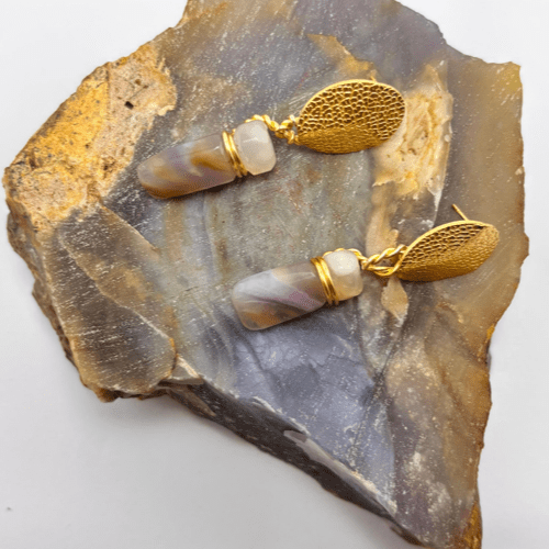 Aretes pilares de aurora colgantes con diseño de hoja dorada y piedra cilíndrica jaspeada morada y beige, sobre una roca rústica.